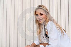 Beautiful young blonde girl with natural healthy skin dressed in white shirt, white wall on the background