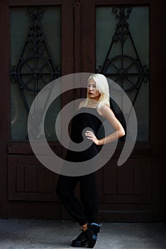 Beautiful young blonde girl posing on the background of Burgundy doors. woman in a black dress. The girl on the background.