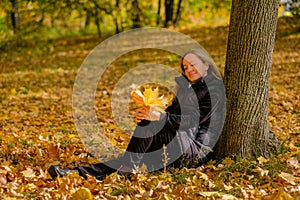 A beautiful young blonde girl sits on fallen autumn leaves in the park