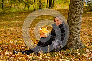 A beautiful young blonde girl sits on fallen autumn leaves in the park