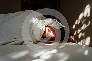 Beautiful, young blonde lies on the bed in the rays of soft, morning sun. Buried under the covers, showing out small part of her