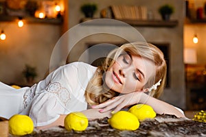 A beautiful young blonde is lying on a bed with her eyes closed in a country house. Near flowers and lemons. Natural beauty