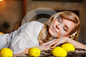 A beautiful young blonde is lying on a bed with her eyes closed in a country house. Next to the lemons. Natural beauty