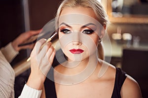 Beautiful young blonde. Makeup artist makes a stylish makeup.