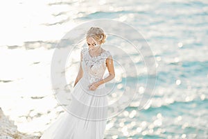 Beautiful young blonde model girl, in white lace dress, stands at the sea coast