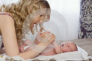 Beautiful young blonde mother is playing with her newborn baby in bed. Mom and her Child. Early development of an