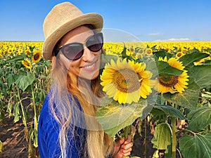 A beautiful young blonde woman in a blue T-shirt, wearing hat, enjoy nature in the sunflower field at sunrise