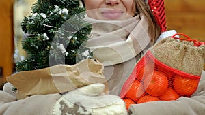 A beautiful young blonde woman at a Christmas fair. The woman is holding a small Christmas tree and brightly coloured