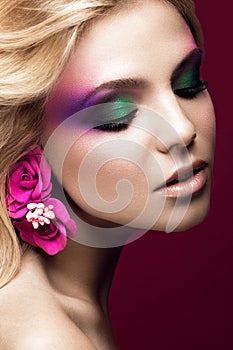 Beautiful young blonde woman with creative make-up color and flowers on the ears. Beauty face. Art makeup.