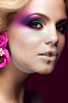 Beautiful young blonde woman with creative make-up color and flowers on the ears. Beauty face. Art makeup.