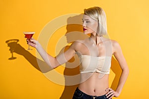 beautiful young blonde woman in denim shorts and top holding glass with cocktail