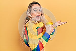 Beautiful young blonde woman drinking cup of coffee wearing headphones pointing aside with hands open palms showing copy space,