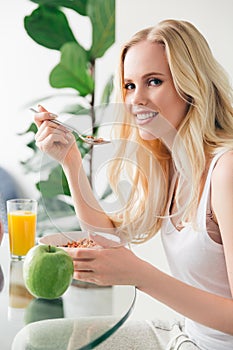beautiful young blonde woman eating muesli for breakfast and smiling