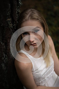 Close up portrait - Beautiful young blonde woman forest nymph in white dress in evergreen wood