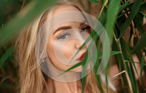 Beautiful young blonde woman among the grass, and strictly looks at the camera, closeup portrait, big eyes