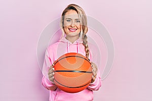 Beautiful young blonde woman holding basketball ball smiling with a happy and cool smile on face