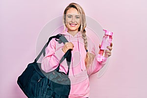 Beautiful young blonde woman holding gym bag and water bottle smiling with a happy and cool smile on face