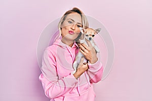 Beautiful young blonde woman hugging cute chihuahua dog looking at the camera blowing a kiss being lovely and sexy