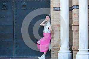 Beautiful young blonde woman leaning on the doorjamb of a large door of a monumental building in the city of Seville. The girl