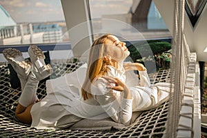 Beautiful young blonde woman lies on a stretched net with sun lights on sunny day.