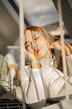 Beautiful young blonde woman lies on a stretched net with sun lights on sunny day.