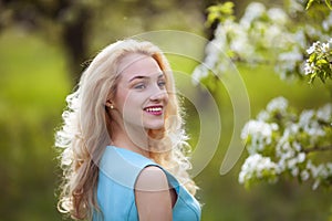 Beautiful young blonde woman looks around, smiling.Portrait of a girl in a flowered garden