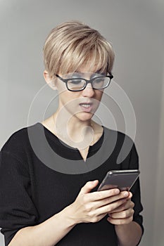 Beautiful young blonde woman looks emotionally at the smartphone
