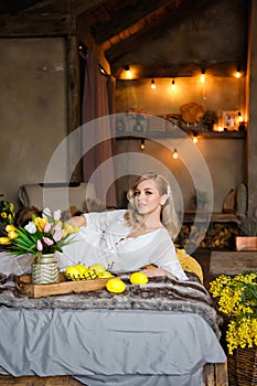 Beautiful young blonde woman lying on a bed in a country house. Near flowers and lemons. Natural beauty