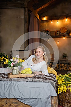 Beautiful young blonde woman lying on a bed in a country house. Near flowers and lemons. Natural beauty