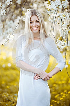 Beautiful young blonde woman in the park with white flowers on a
