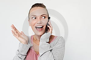 A beautiful young blonde woman picks up the news on the phone and is surprised. Great news! Over white background.