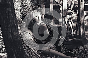 Beautiful young blonde woman sitting near the hay in the yard in rural areas. black-white