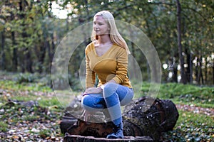 Young blonde woman sitting on a tree branch in the forest