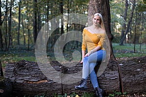 Young blonde woman sitting on a tree branch in the forest