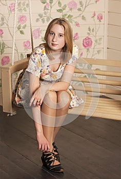 Beautiful young blonde woman sitting in a trendy shoes and white dress