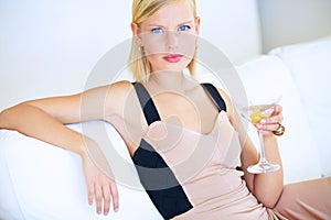 Shes a Bond-girl in the making. Beautiful young blonde woman sitting on a white couch drinking a martini.