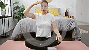 Beautiful young blonde woman stretching her neck on bedroom floor for morning yoga, a calming exercise for wellness and balance