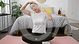 Beautiful young blonde woman stretching her neck on bedroom floor, waking up with a smile, immersed in relaxing yoga