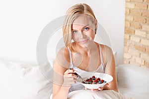 Beautiful young blonde woman waking up and eating oatmeal with berries in the morning