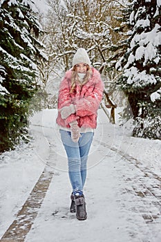 A beautiful young blonde woman walks along a path in the park in winter.