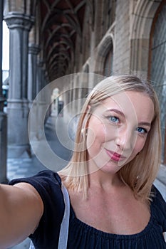 Beautiful young blonde woman wearing a black blouse and smiling confident making a selfie using a smartphone in the