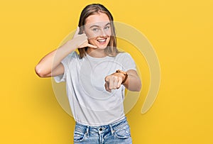 Beautiful young blonde woman wearing casual white t shirt smiling doing talking on the telephone gesture and pointing to you