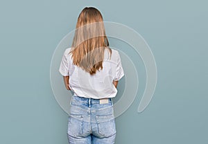 Beautiful young blonde woman wearing casual white t shirt standing backwards looking away with crossed arms