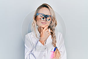 Beautiful young blonde woman wearing optometry glasses thinking concentrated about doubt with finger on chin and looking up