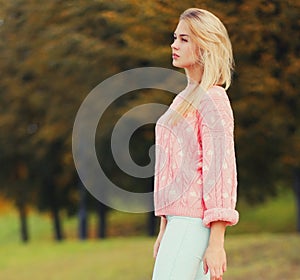Beautiful young blonde woman wearing a pink knitted sweater in a city park