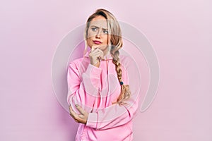 Beautiful young blonde woman wearing pink sweatshirt thinking concentrated about doubt with finger on chin and looking up