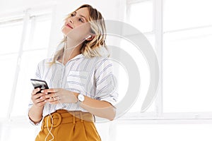 Beautiful young blonde woman wearing shirt listening to music