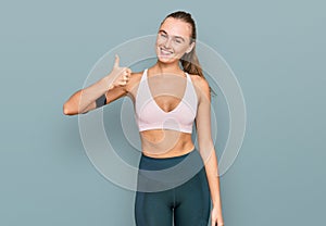 Beautiful young blonde woman wearing sportswear and arm band smiling happy and positive, thumb up doing excellent and approval