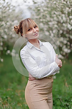 Beautiful young blonde woman in white shirt posing under apple tree in blossom in Spring garden