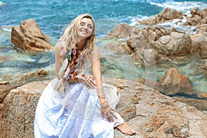 Beautiful young boho style woman in white dress on stone beach